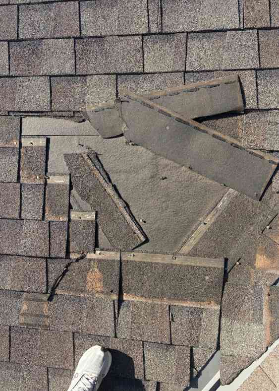 lawton roofer standing on roof inspecting wind damage on residential home with brown shingles