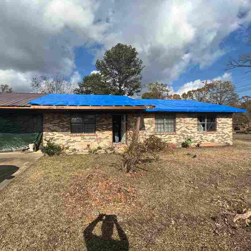 contractor placing blue tarp on roof to cover hole and protect home after tornado damage