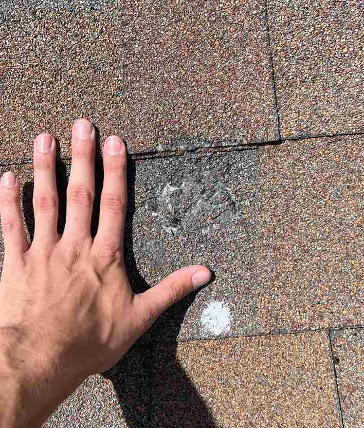 roofing contractor pointing to hail impact damage on asphalt roof shingle