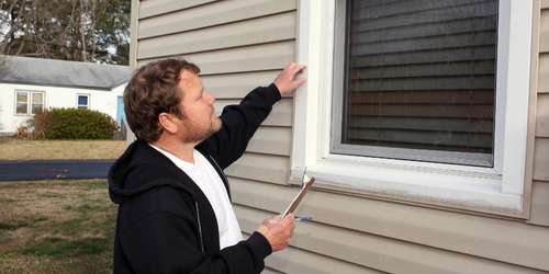 man holding clipboard going through items on hail damage inspection checklist outside of home