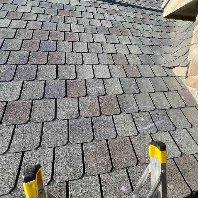 contractor on ladder taking close up photo of roof during inspection in Stillwater, OK