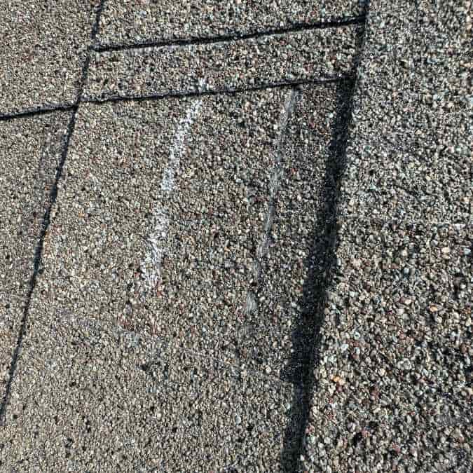 close up of crease in asphalt shingle after wind damage has blown it back and broken the seal