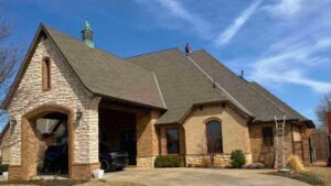 roofer on top of residential home performing inspection discussing top roofing challenges in Oklahoma City with homeowner